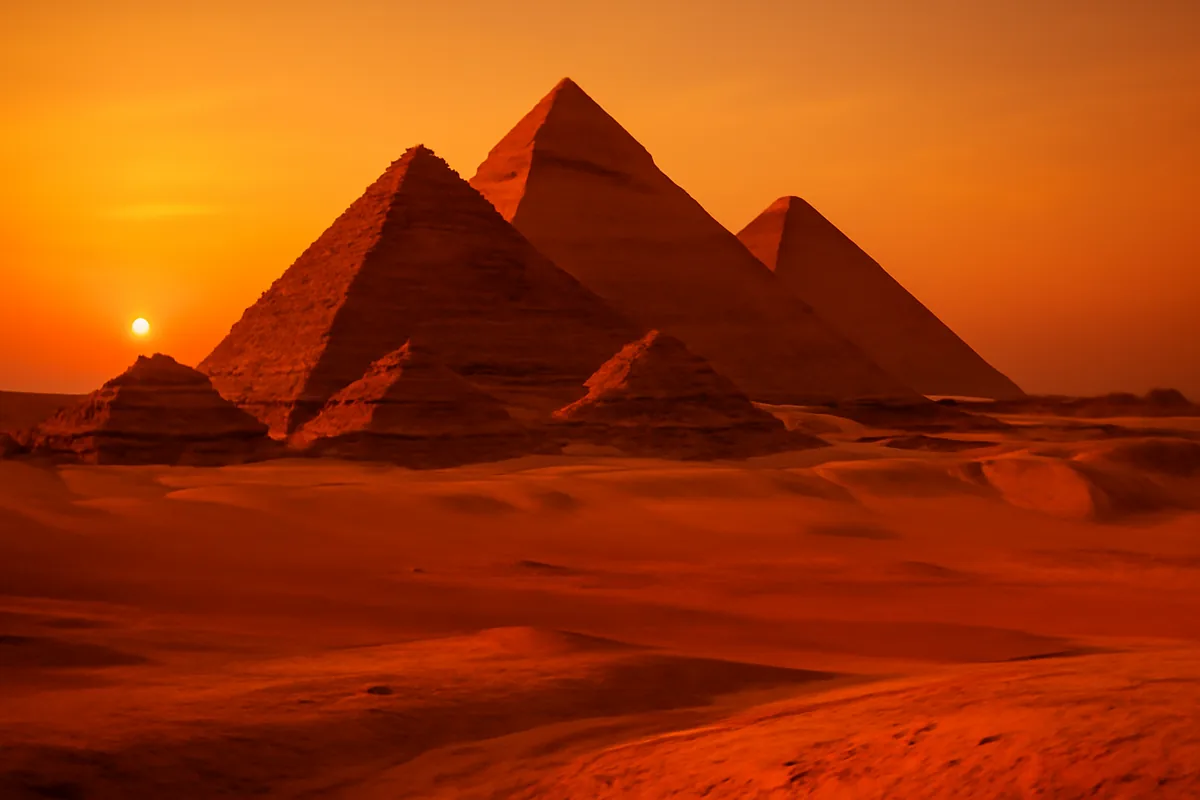 The pyramids of Giza at sunset, surrounded by golden desert sands under a warm orange sky