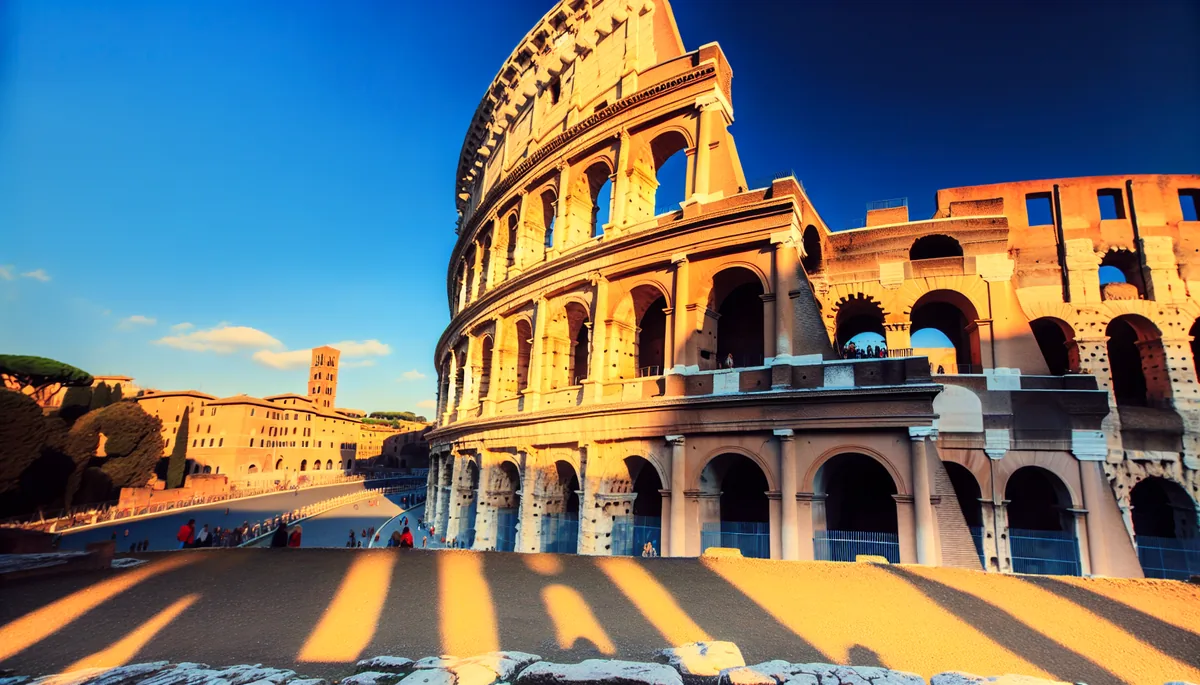 Golden hour view of the Roman Colosseum with warm sunlight illuminating the ancient stone architecture and small silhouettes of tourists exploring the historic amphitheater