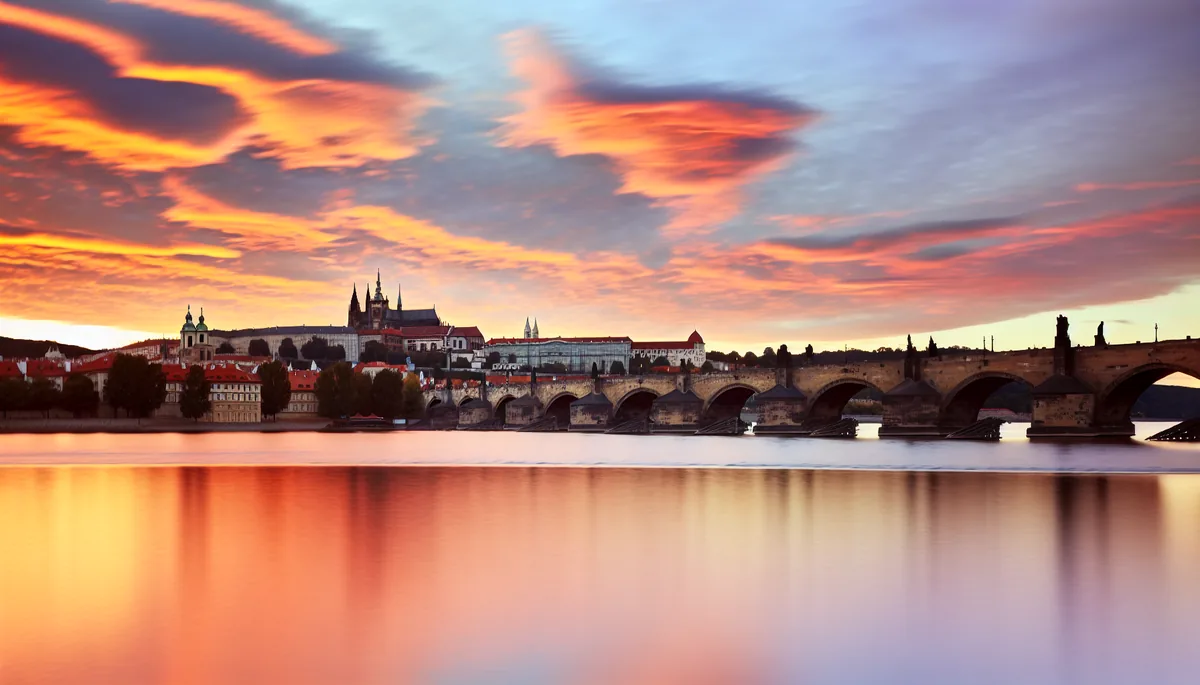 Panoramic view of Prague Castle and Charles Bridge at sunset with the Vltava River reflecting golden light