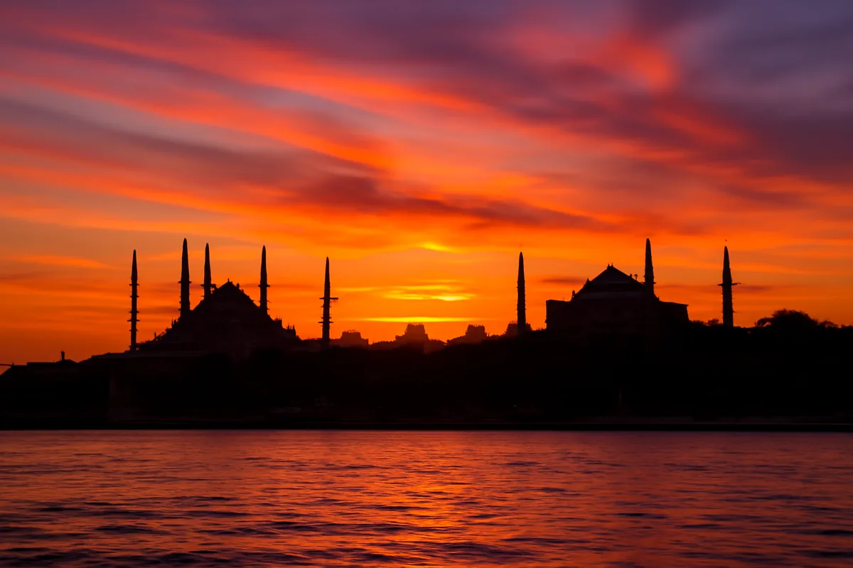 Stunning sunset view of Istanbul's historic skyline featuring the Blue Mosque and Hagia Sophia reflected in the Bosphorus waters