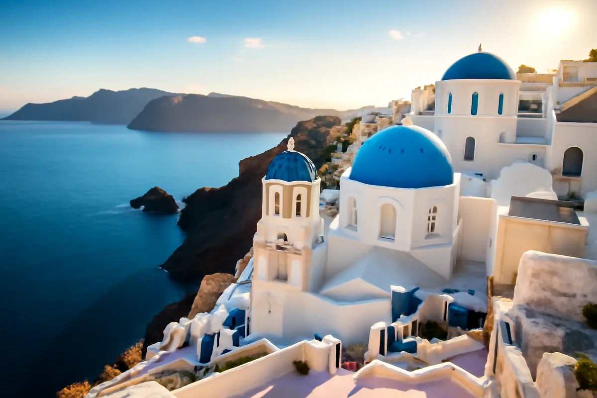 Scenic Mediterranean coastal village with white buildings and blue domes overlooking crystal clear blue waters during golden hour