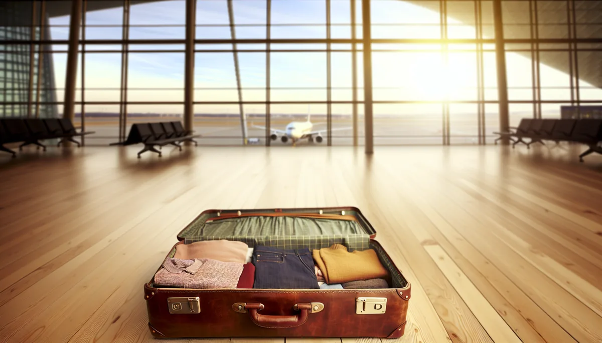 Open vintage leather suitcase with neatly organized travel clothes and essentials, with Copenhagen airport terminal softly blurred in the background through large windows