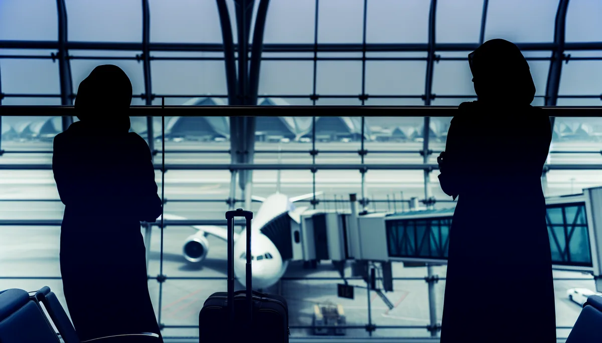 Silhouette of a traveler at an airport departure gate with planes visible through large windows under an overcast sky