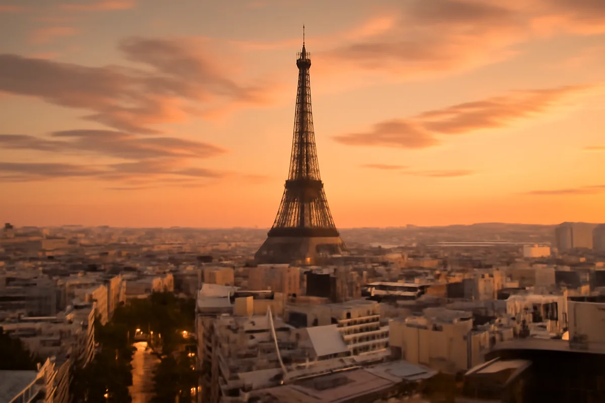 Golden hour view of the Eiffel Tower towering above classic Parisian rooftops and glowing boulevards at dusk