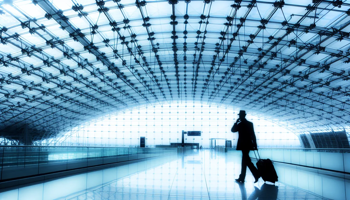 Silhouette of a traveler walking through a modern airport terminal with large windows and contemporary architecture