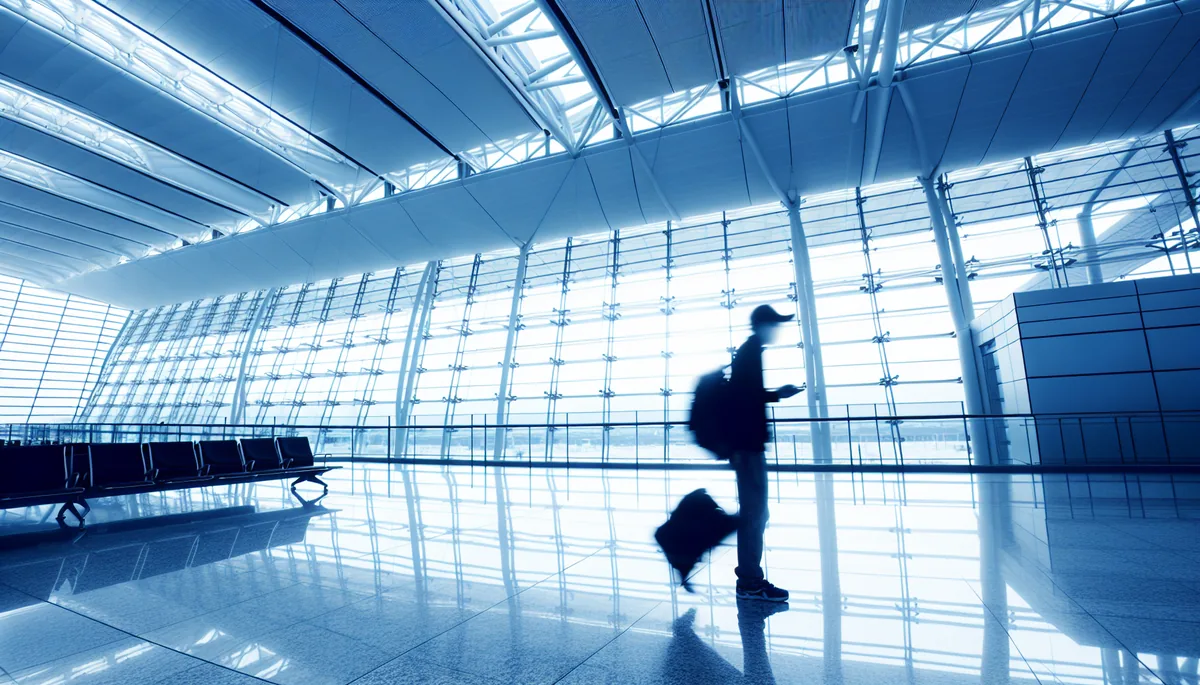 Silhouette of a traveler walking through a modern airport terminal with large glass windows and contemporary architecture