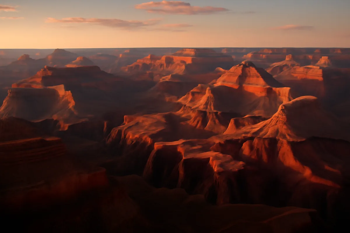 A breathtaking panoramic view of the Grand Canyon at golden hour, with dramatic layered red and orange rock formations illuminated by warm sunlight stretching endlessly into the horizon.