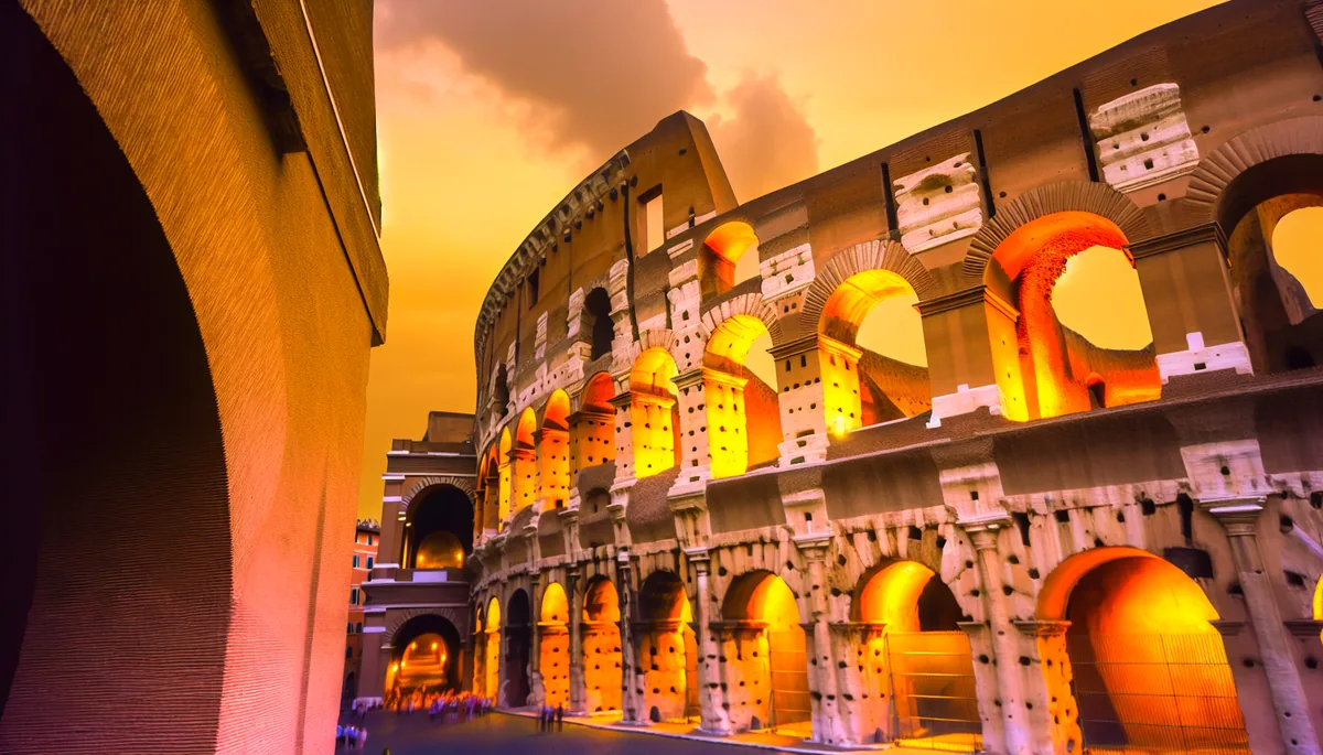 Golden hour view of the Roman Colosseum with warm lighting illuminating the ancient stone architecture and small silhouettes of tourists exploring the historic site