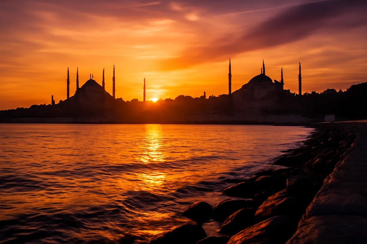 Stunning sunset view of Istanbul's historic skyline featuring the Hagia Sophia and Blue Mosque silhouettes reflected in the Bosphorus strait