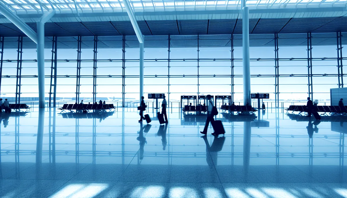 Modern airport terminal interior with travelers walking toward departure gates, featuring large windows and contemporary architecture