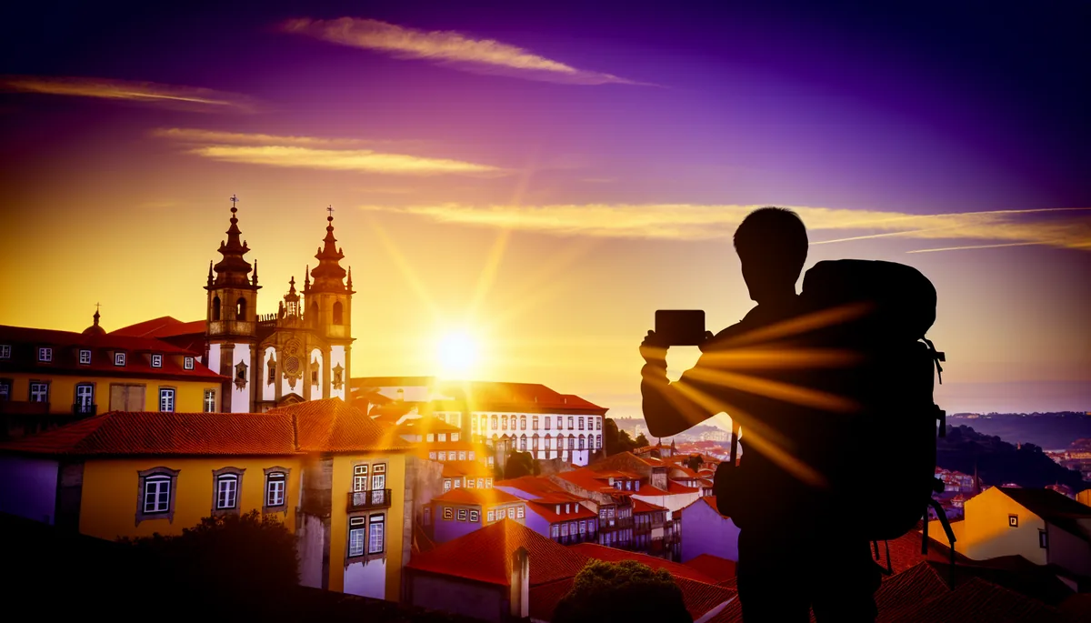 Silhouette of a traveler looking out over a European city with traditional red-tiled roofs and historic architecture during golden hour sunset