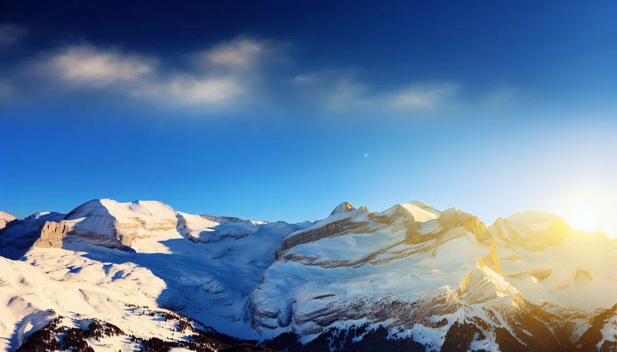 Breathtaking panoramic view of snow-covered Alpine mountain peaks with golden sunlight and clear blue sky
