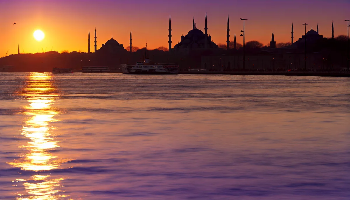 Panoramic view of Istanbul's historic skyline at sunset, featuring the silhouettes of the Blue Mosque and Hagia Sophia with the Bosphorus strait reflecting golden light