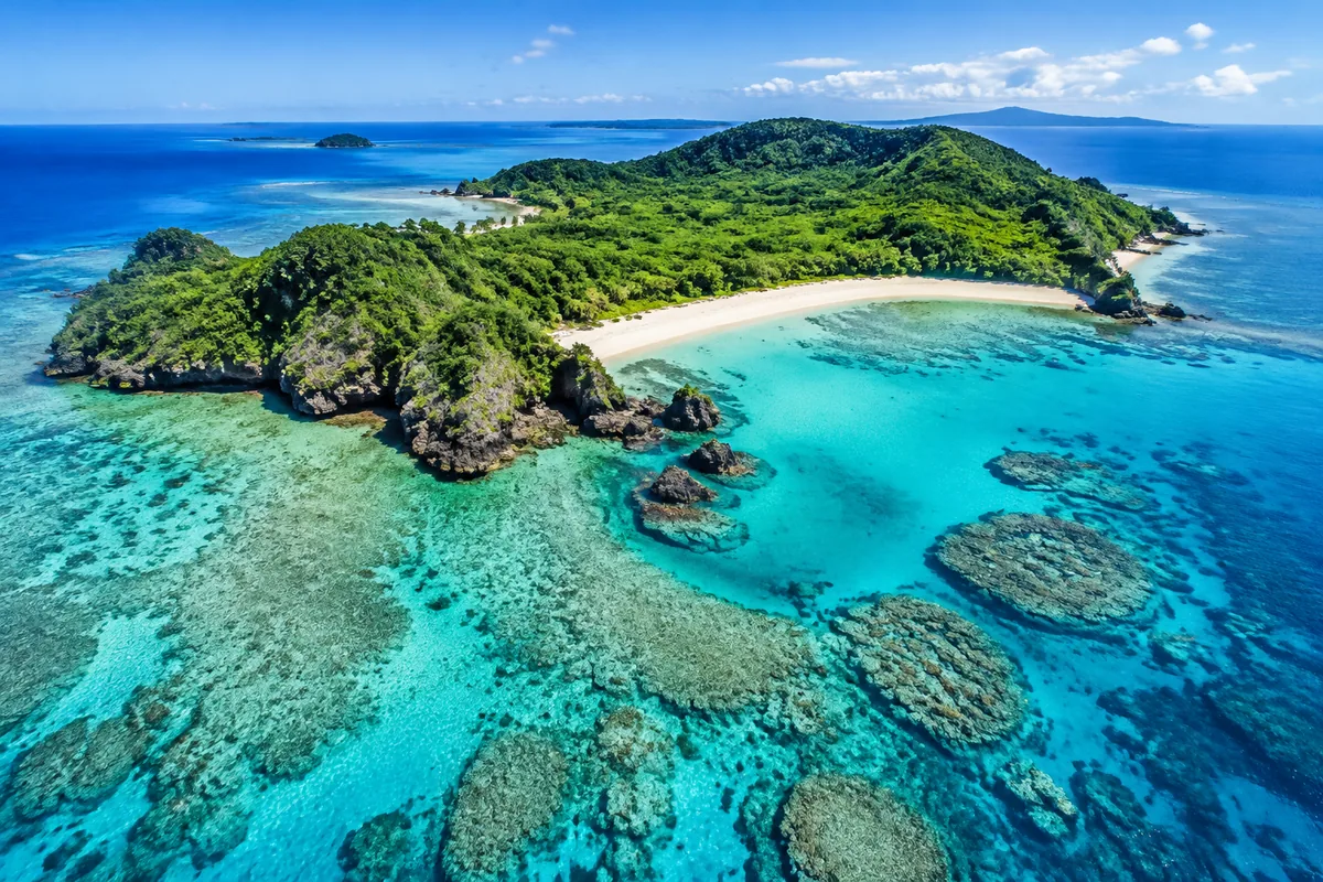 Aerial view of a pristine tropical island in the Okinawa archipelago, surrounded by turquoise coral reef waters and white sandy beaches under bright sunlight